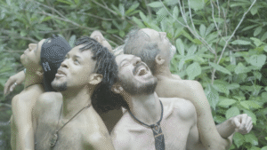A circle of men participating in a mindful movement and embodiment practice beneath tall trees in a peaceful forest.