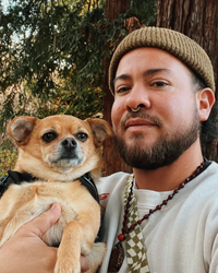 headshot of andres gonzales trans meditation teacher holding their little dog