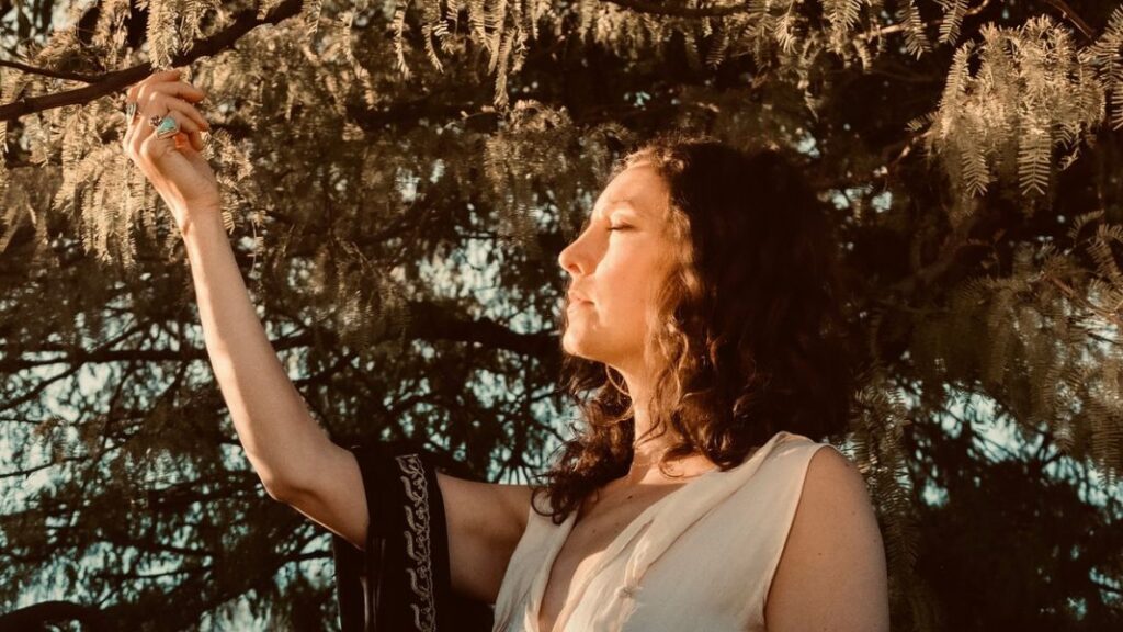 Heather Wolf with eyes closed reaching for a tree branch