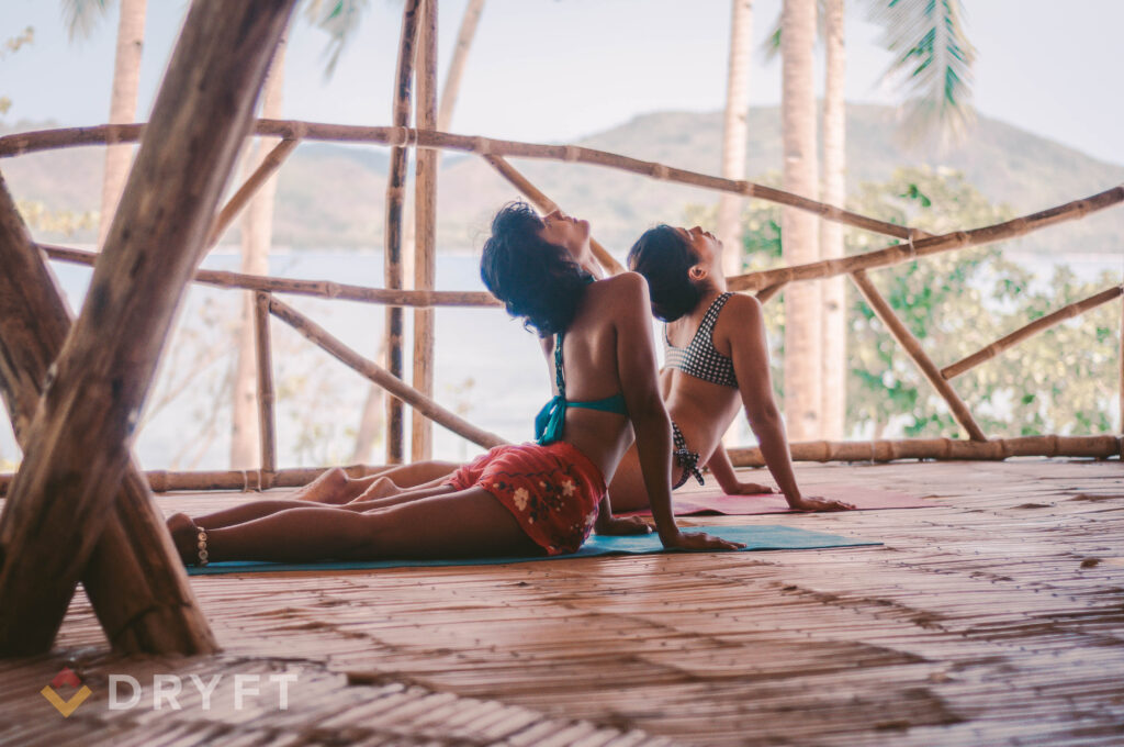 2 people practicing yoga on a bamboo deck at DRYFT