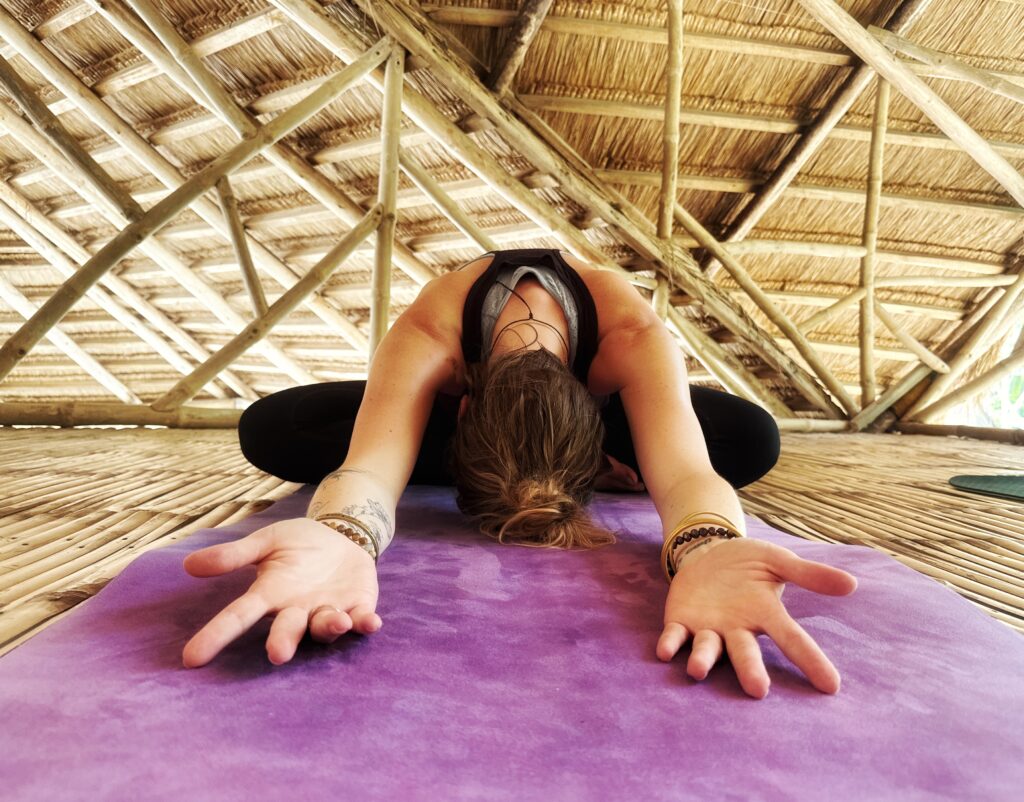 Female yoga practitioner in seated forward fold pose and arms outstretched, in bamboo structure