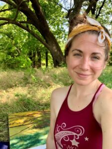 Liz outside in the woods with a painting