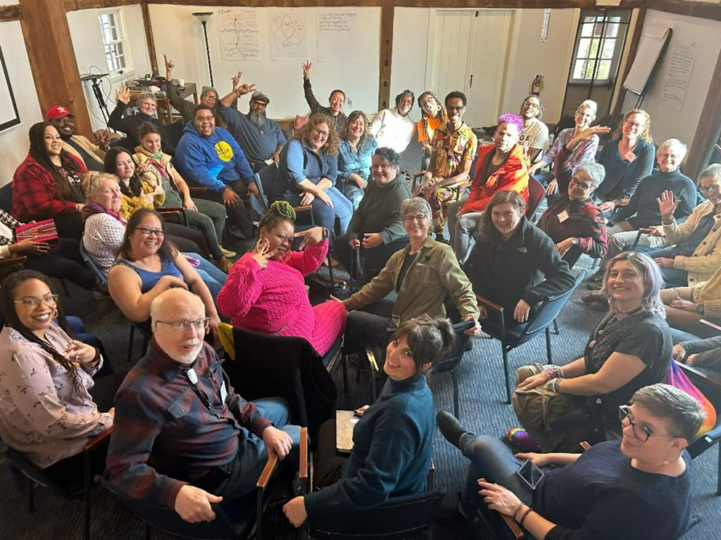 A group photo from a Beyond Diversity 101 training. A mix of people sit in circles of chairs with chart paper notes on the walls.