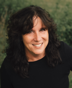 A headshot of a smiling white woman with dark hair in front of a green background.