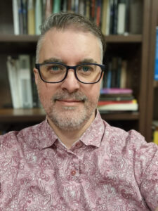 A white person with short hair and glasses in a pink shirt.