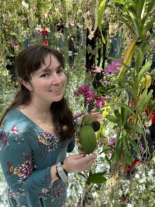 A white woman with dark hair in front of colorful plants.