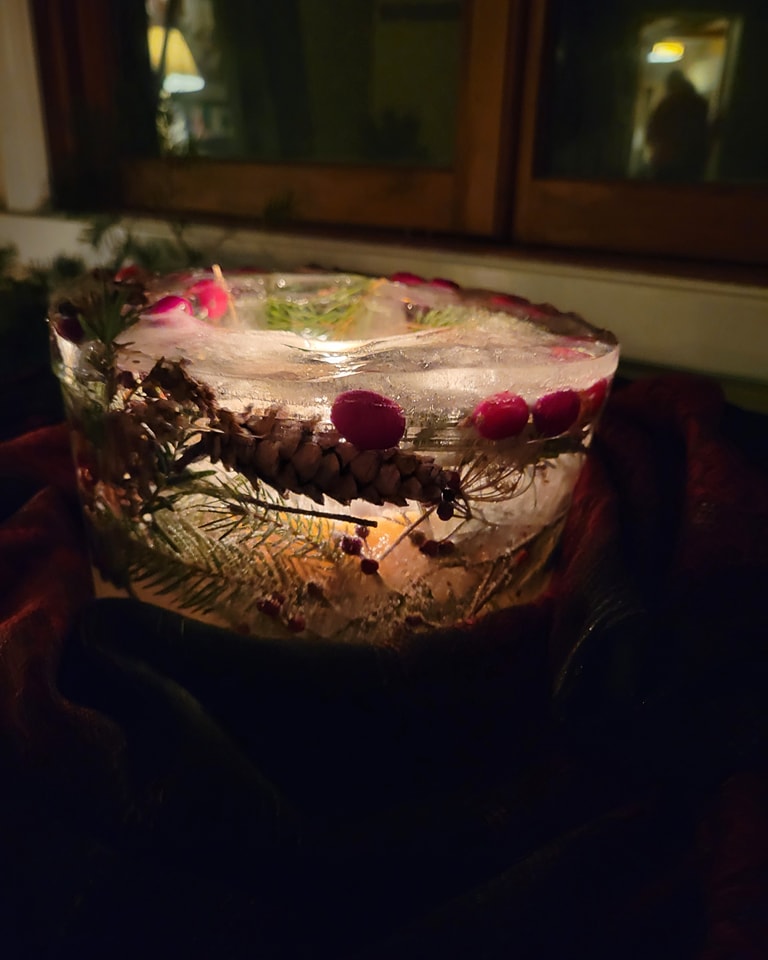 A round centerpiece made of ice and frozen branches and berries glows from a candle inside.