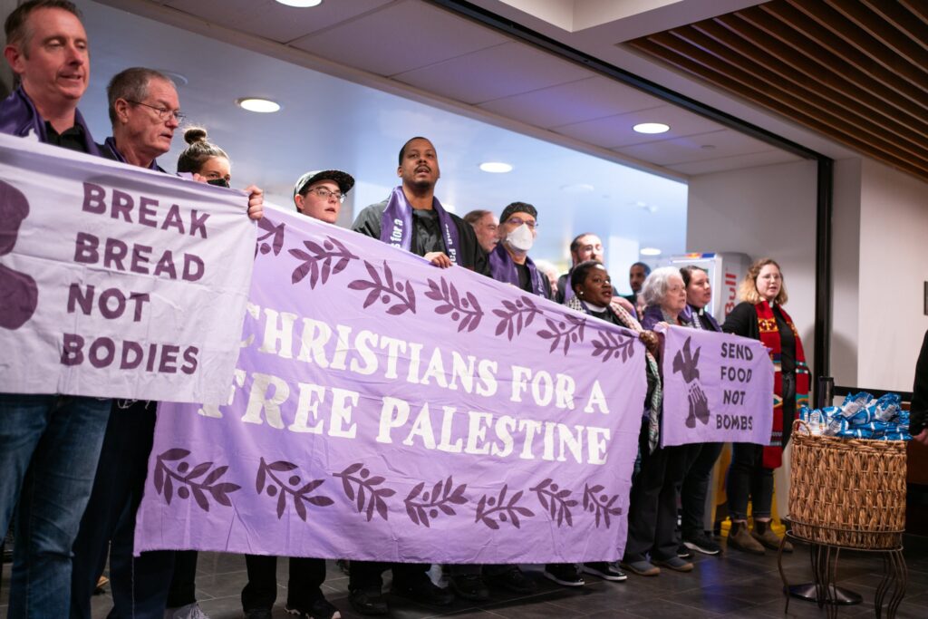 A line of people hold three banners that read "Break Bread not Bodies" and "Christians for a Free Palestine."