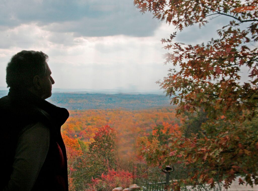 A backlit man in profile in front of an autumnal vista.