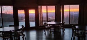 The Nelson Lodge dining room with windows facing an orange, yellow, pink sunset.