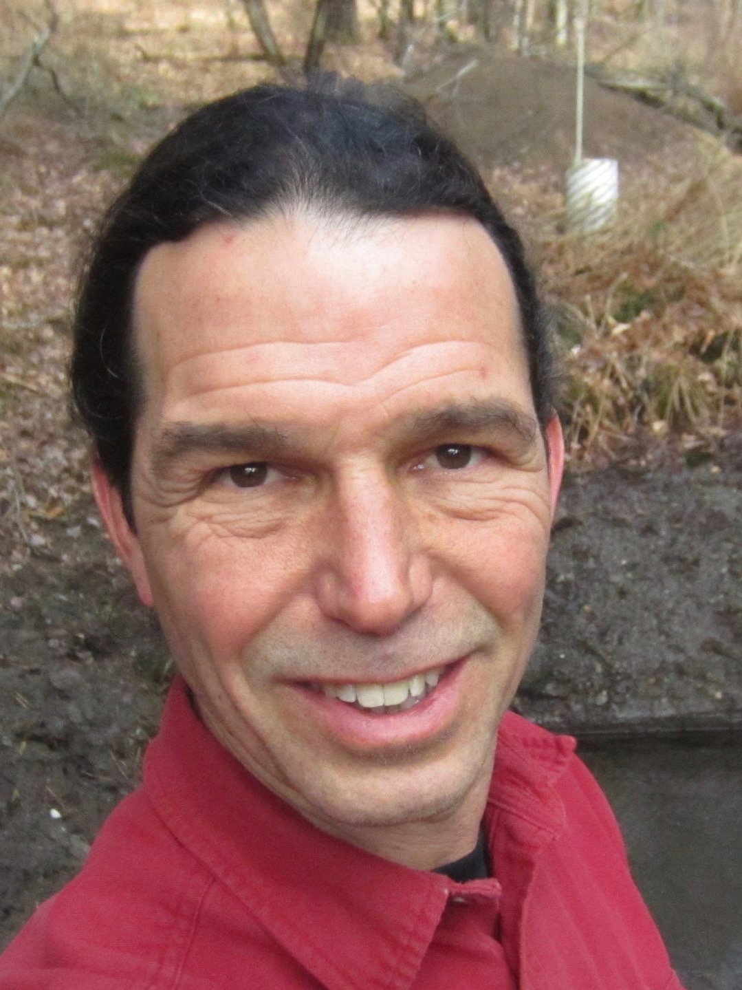 man with dark hair, ponytails and red collared shrir