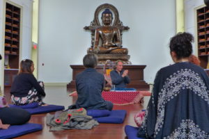 Man teaches a group with a Buddha statue behind him