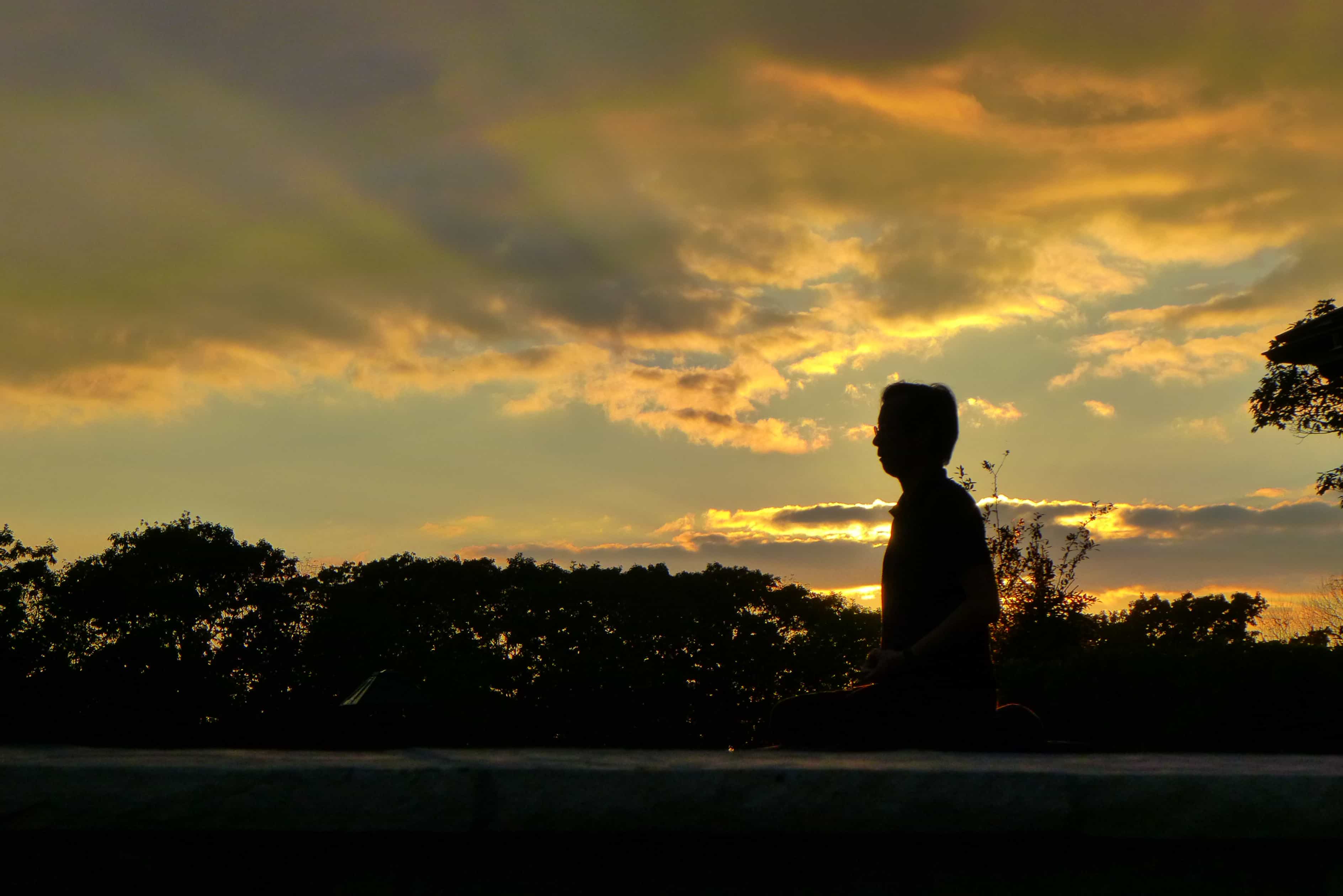 Seated man silhouetted at sunset