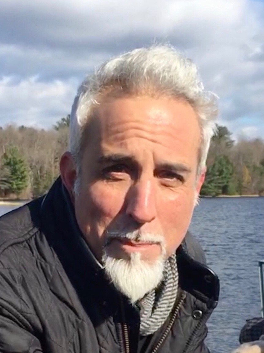 Man with white hair and white beard with the water behind him