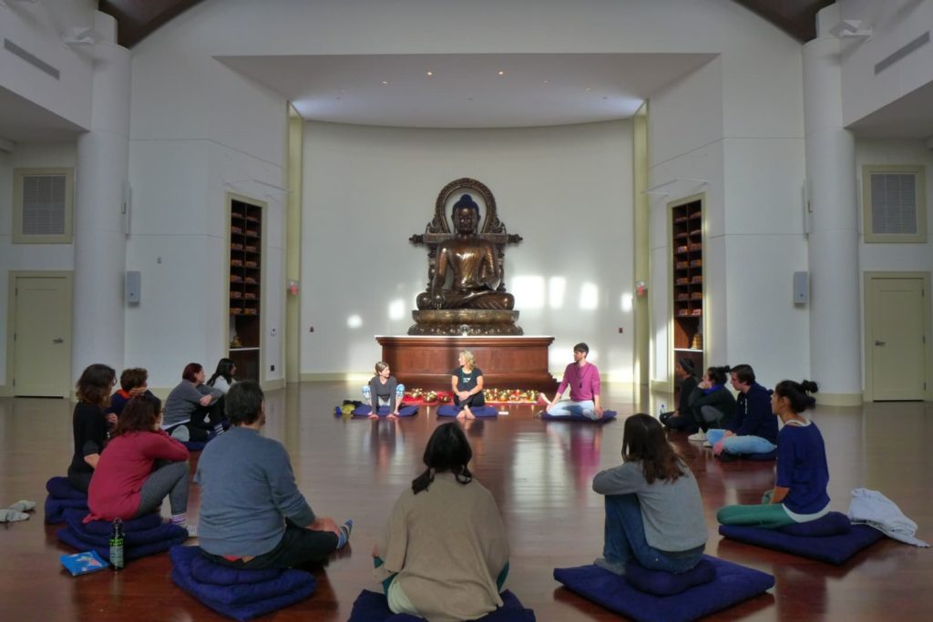 people sit in a large circle in a light filled room with a large Buddha