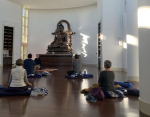 a group of peopel sit in meditation in front of a large statue of Buddha