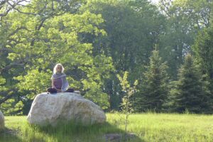woman practices outdoor meditation on top of a rock