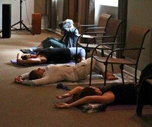 A few people lying down in the Sanctuary Learning Center doing a twist yoga pose.